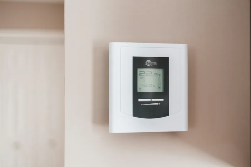 A white programmable thermostat with a small display on a wall