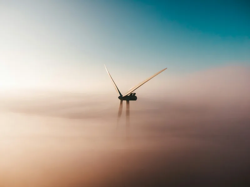 A wind turbine emerging from the fog at dawn