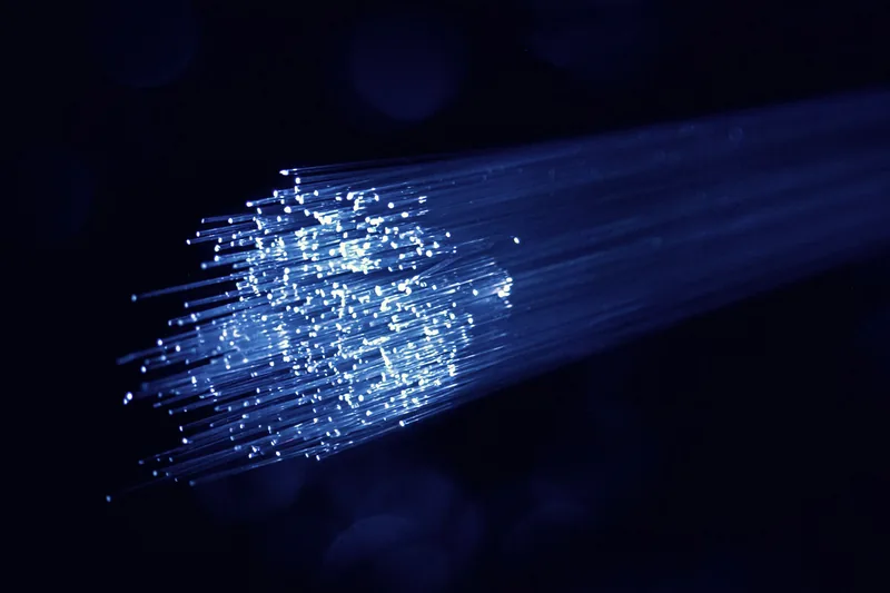 Strands of optical fibre glowing white and blue in the dark