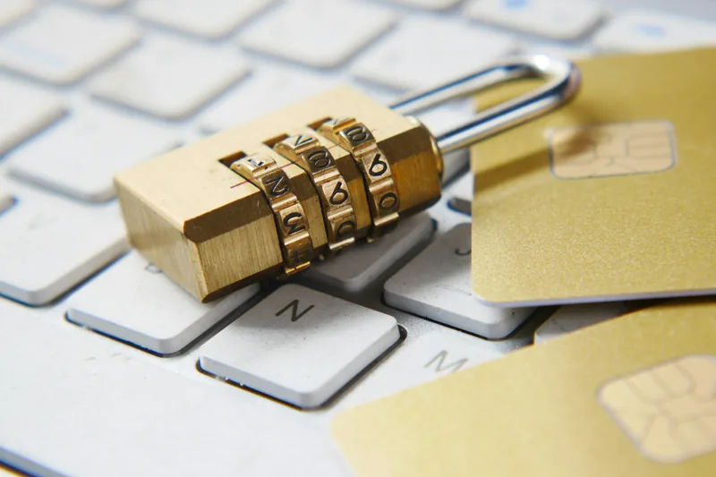 A brass combination padlock resting on a keyboard next to payment cards