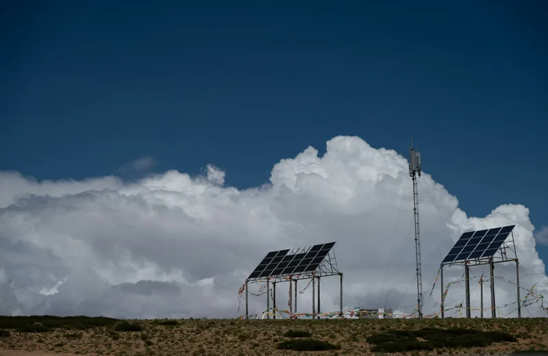 Solar panels and a telecommunications tower under a cloudy sky