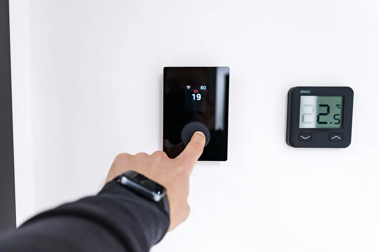 A hand adjusting a digital wall thermostat