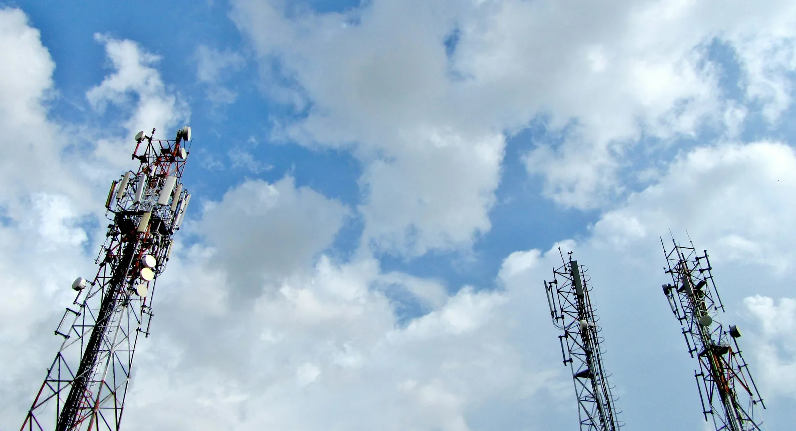 Several cellular towers against a cloudy blue sky